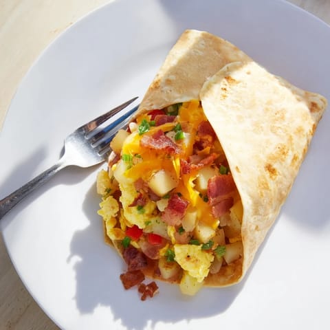 A plated Breakfast Burrito sliced in half, revealing layers of sausage, peppers, onions, and gooey cheddar cheese.