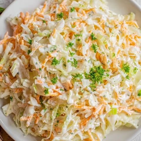 Freshly prepared Coleslaw with Apple salad topped with parsley, served chilled alongside a sandwich for a light and tangy American side dish.