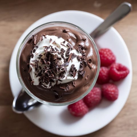 Luscious homemade chocolate pudding served chilled in a glass, garnished with fresh raspberries and mint.