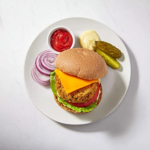 Veggie burger with golden-brown patty, melty cheddar, red onion rings, and pickles on a toasted whole wheat bun served with ketchup.