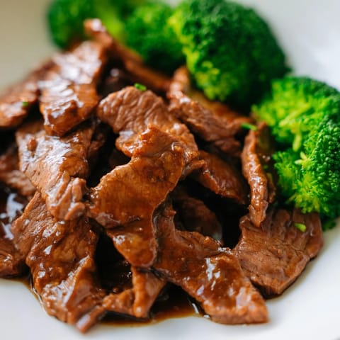 Sizzling Beef and Broccoli in a wok with minced garlic and ginger, steam rising as the beef sears alongside crisp broccoli.