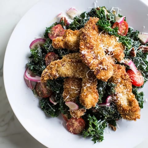 A close-up of Crispy Chicken Kale Salad shows crunchy panko-coated chicken over massaged kale, pecans, and cherry tomatoes with glistening dressing.