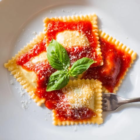 Spinach ricotta ravioli, freshly prepared, served in a rich red marinara sauce on a plate.  