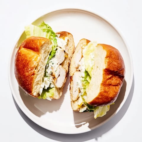 A fully assembled Caesar Chicken Sandwich shows juicy grilled meat, fresh greens, and shaved Parmesan on a soft, buttery bun.