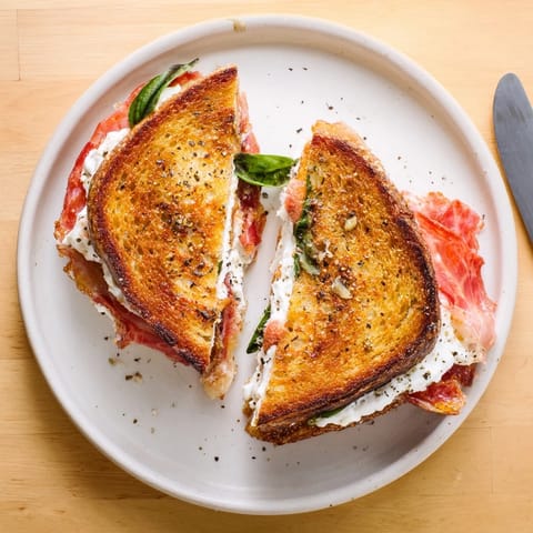 A close-up of Crispy Prosciutto & Burrata Grilled Cheese served with fresh basil on a rustic board.