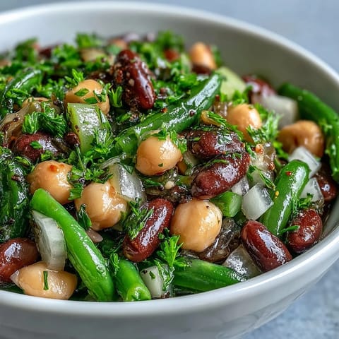 A vibrant Three-Bean Salad with chickpeas, kidney beans, and green beans tossed in a tangy apple cider vinaibrette.