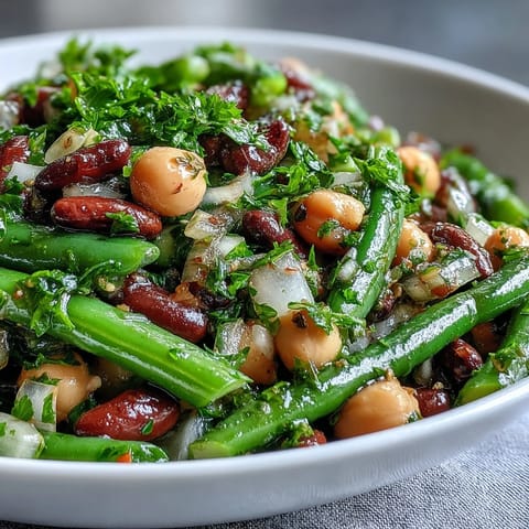This chilled Three-Bean Salad in a white bowl features crunchy celery and red onion, a perfect vegetarian side dish.