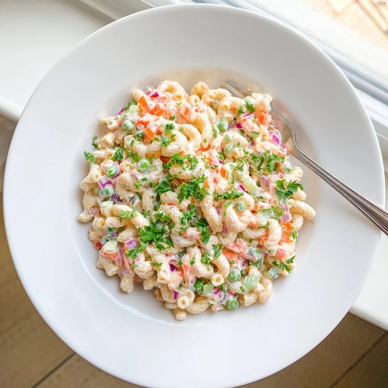 Cold Macaroni Salad featuring tender elbow pasta, crisp vegetables, and creamy mayonnaise garnished with fresh parsley.