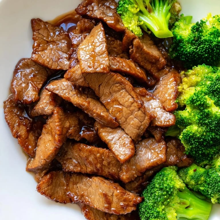 Served family-style, Beef and Broccoli is plated over fluffy jasmine rice and topped with sesame seeds and sliced green onions.