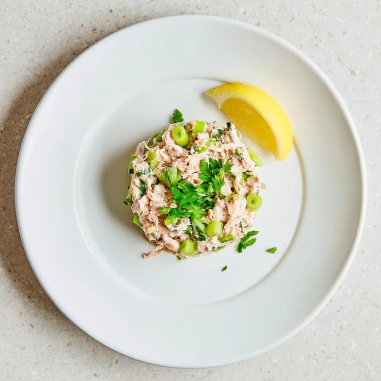 Close-up view of zesty tuna salad ingredients including canned tuna, mayonnaise, and hot sauce, mixed in a ceramic bowl for a quick lunch.