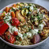 Golden-brown roasted vegetables over fluffy quinoa in a bowl, generously drizzled with creamy tahini sauce.