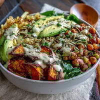 Golden roasted sweet potato cubes and crispy chickpeas in a bowl with garlicky spinach, topped with creamy smoky chipotle tahini dressing.